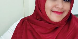 Stella Putri mengenakan hijab merah tersenyum ke arah kamera